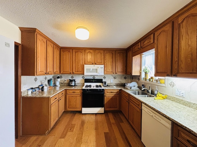 kitchen with sink, light wood-type flooring, white appliances, light stone counters, and a textured ceiling