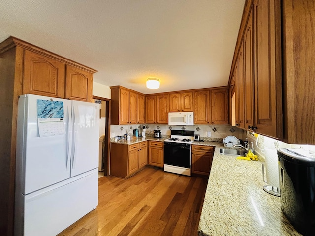 kitchen with sink, light stone counters, a textured ceiling, white appliances, and hardwood / wood-style floors