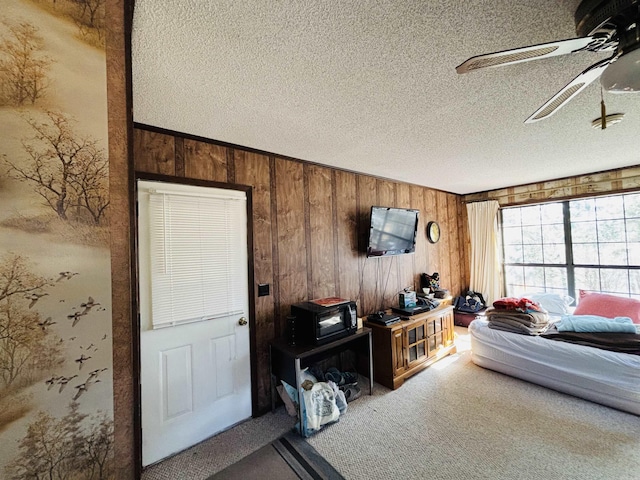 carpeted living room featuring ceiling fan, wooden walls, and a textured ceiling