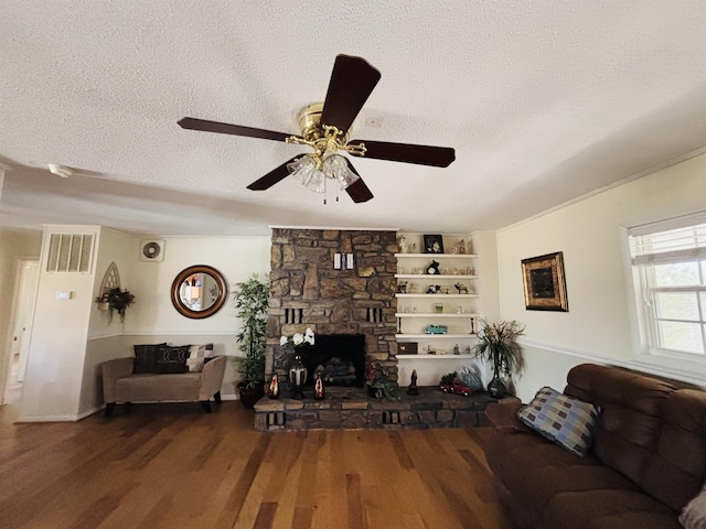 living room featuring built in features, ceiling fan, dark hardwood / wood-style floors, a textured ceiling, and a stone fireplace