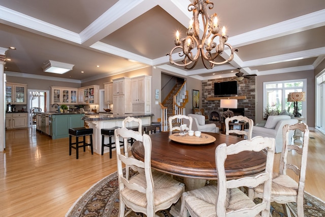 dining space with beamed ceiling, a large fireplace, a notable chandelier, crown molding, and light wood-type flooring