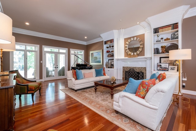 living room featuring french doors, ornamental molding, built in features, a premium fireplace, and hardwood / wood-style floors