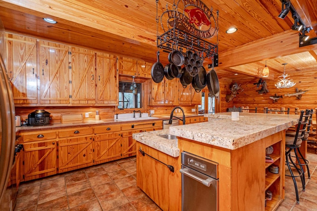 kitchen featuring a kitchen island with sink, sink, wooden ceiling, and wood walls