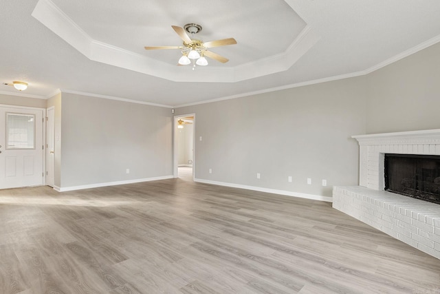 unfurnished living room featuring light hardwood / wood-style flooring, ceiling fan, a fireplace, ornamental molding, and a raised ceiling