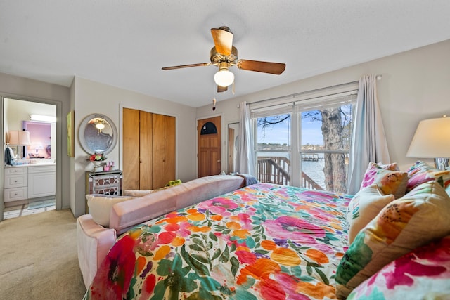 bedroom with light carpet, ensuite bath, ceiling fan, and a water view