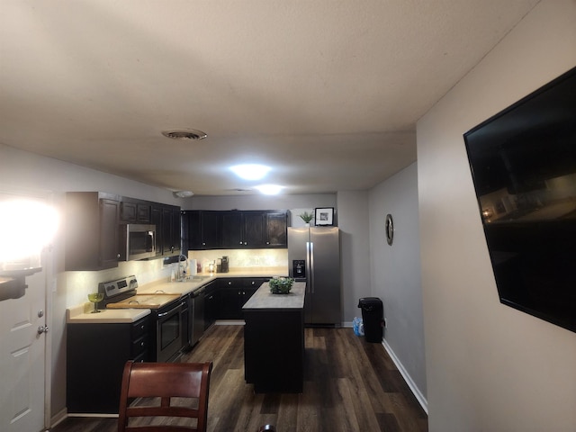 kitchen featuring visible vents, a kitchen island, dark wood-type flooring, stainless steel appliances, and light countertops