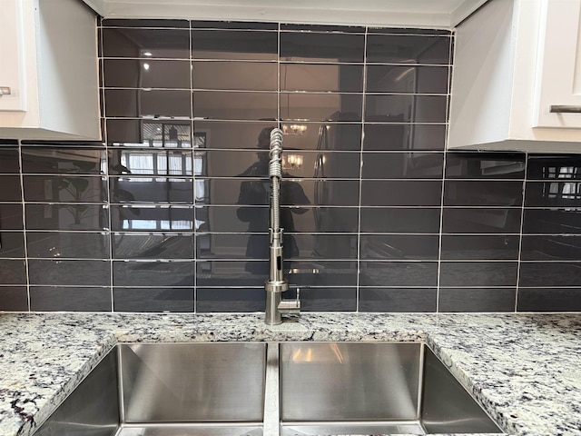 interior details featuring tasteful backsplash, white cabinetry, light stone countertops, and sink