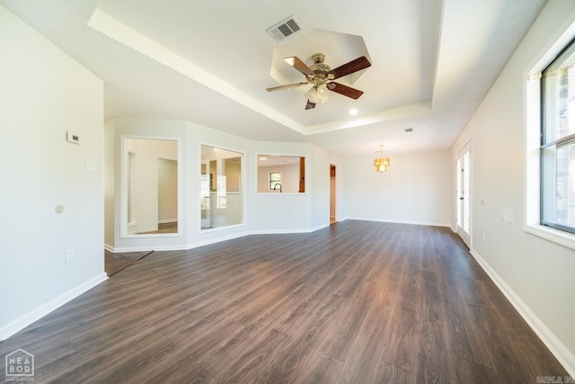 unfurnished living room featuring a tray ceiling, dark wood-type flooring, and ceiling fan with notable chandelier