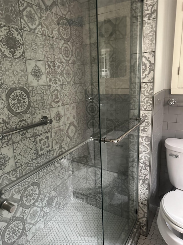 bathroom with tile walls, tile patterned flooring, a shower with shower door, and toilet