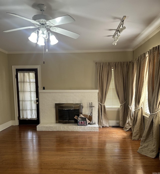 unfurnished living room with crown molding, rail lighting, ceiling fan, hardwood / wood-style floors, and a brick fireplace