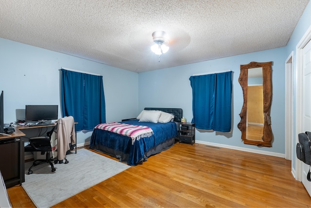 bedroom with hardwood / wood-style flooring, ceiling fan, and a textured ceiling