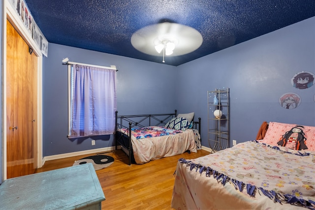 bedroom featuring wood-type flooring, a textured ceiling, ceiling fan, and a closet