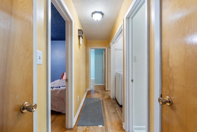 hall with washer / dryer, light hardwood / wood-style flooring, and a textured ceiling