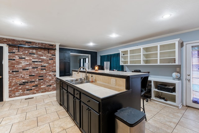 kitchen featuring sink, crown molding, light tile patterned floors, a center island with sink, and brick wall