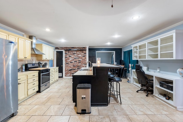 kitchen with a kitchen bar, ornamental molding, stainless steel appliances, a kitchen island with sink, and wall chimney range hood