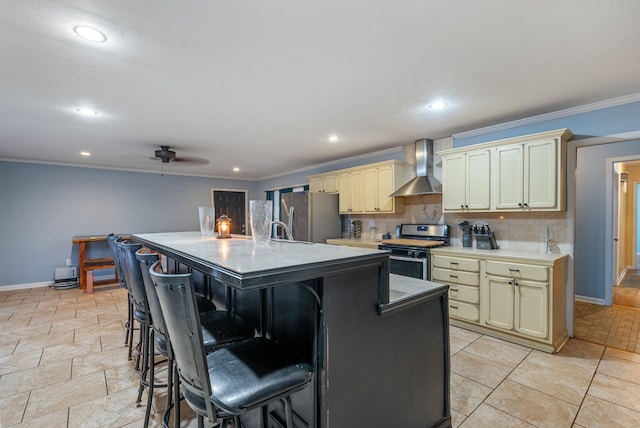 kitchen featuring a breakfast bar area, a kitchen island with sink, stainless steel appliances, cream cabinets, and wall chimney exhaust hood