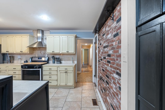 kitchen with gas stove, cream cabinets, wall chimney range hood, and crown molding