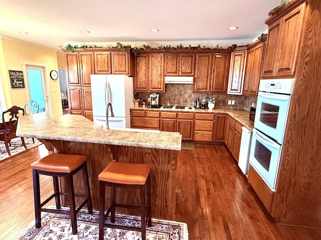 kitchen featuring dark wood-type flooring, tasteful backsplash, ornamental molding, a kitchen breakfast bar, and white appliances