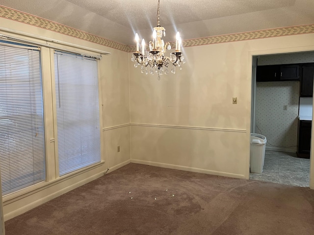 unfurnished dining area with an inviting chandelier, a textured ceiling, and dark colored carpet