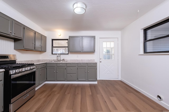 kitchen with light hardwood / wood-style floors, gray cabinets, sink, and stainless steel gas range oven