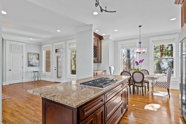 kitchen featuring stainless steel gas cooktop, light stone counters, light wood-type flooring, a notable chandelier, and pendant lighting