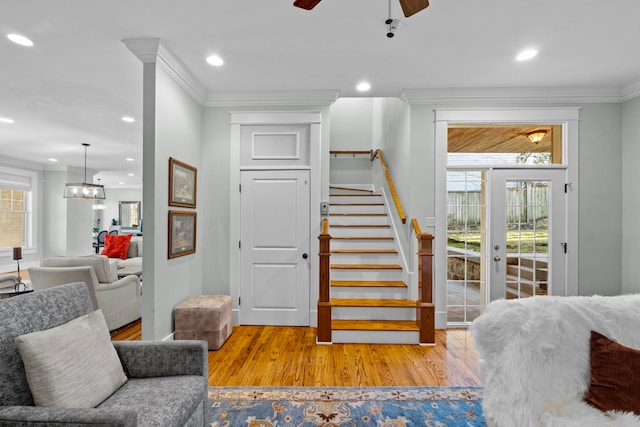 staircase featuring hardwood / wood-style flooring, ornamental molding, and ceiling fan with notable chandelier