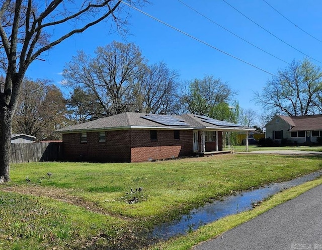 view of side of property with brick siding, solar panels, a lawn, and fence