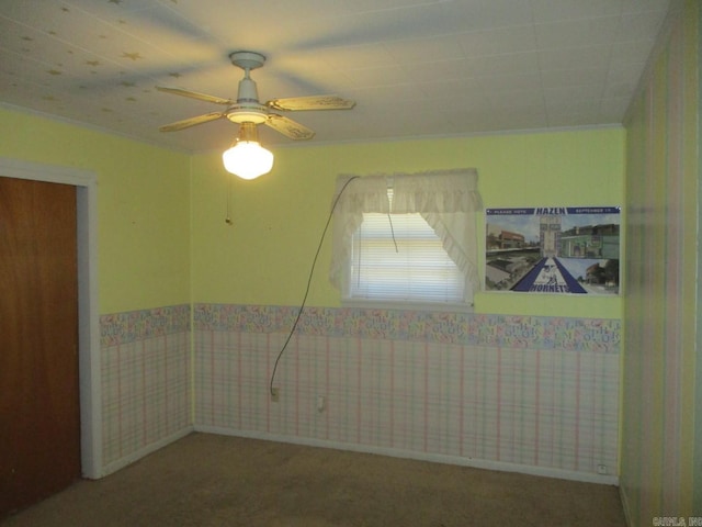 carpeted empty room with wallpapered walls, crown molding, ceiling fan, and wainscoting