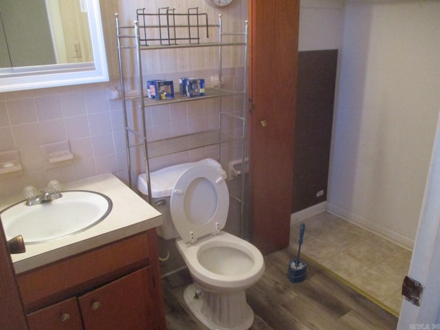 bathroom with toilet, backsplash, tile walls, baseboards, and vanity