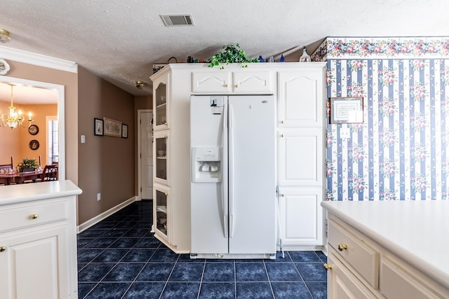 kitchen with white cabinets, dark tile patterned floors, white refrigerator with ice dispenser, a notable chandelier, and a textured ceiling