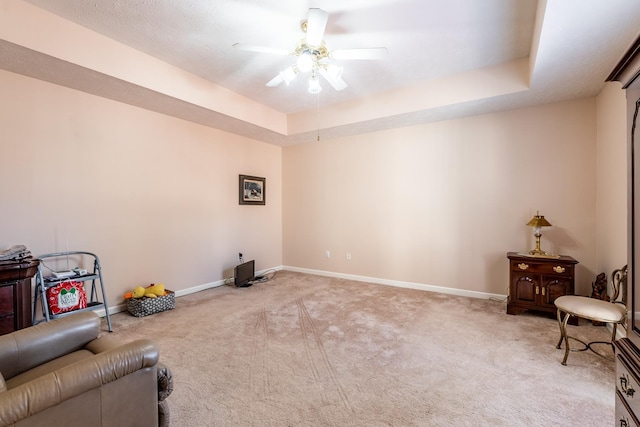 living area featuring carpet, ceiling fan, and a tray ceiling