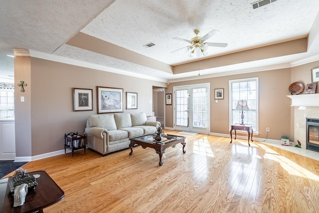 living room with a tile fireplace, a raised ceiling, a textured ceiling, french doors, and light wood-type flooring