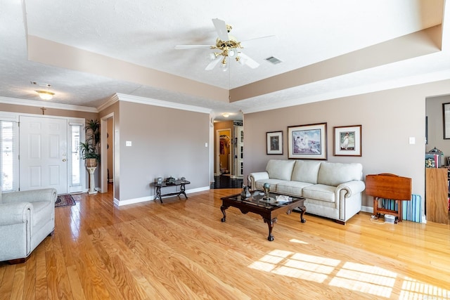 living room with ceiling fan, ornamental molding, a textured ceiling, a raised ceiling, and light wood-type flooring