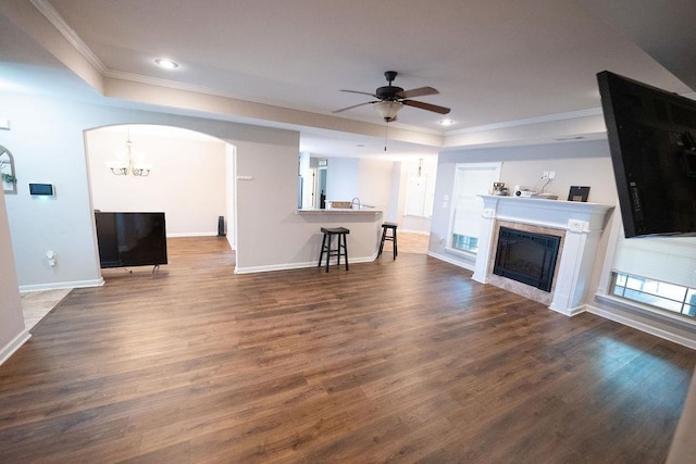 unfurnished living room featuring ornamental molding, ceiling fan with notable chandelier, dark hardwood / wood-style flooring, and a tray ceiling