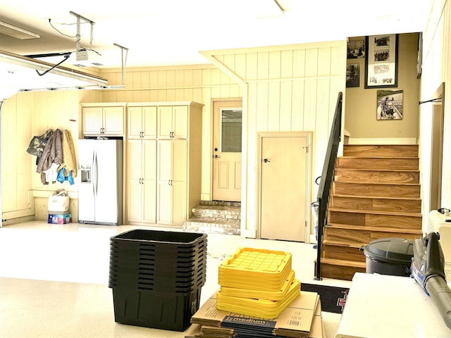 garage with a garage door opener, refrigerator with ice dispenser, and wood walls