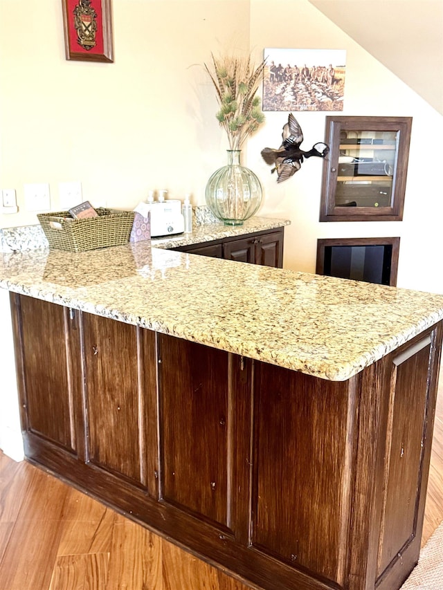 bar with vaulted ceiling, light wood-type flooring, and light stone counters