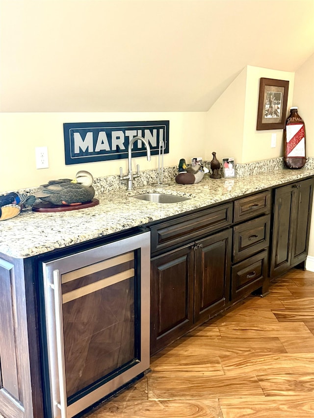 bar featuring dark brown cabinetry, sink, light stone counters, beverage cooler, and light hardwood / wood-style floors