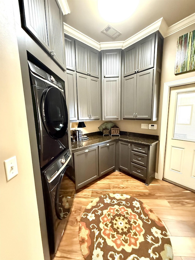 laundry area with cabinets, stacked washer / dryer, crown molding, and light hardwood / wood-style flooring