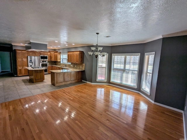 kitchen with appliances with stainless steel finishes, hanging light fixtures, tasteful backsplash, kitchen peninsula, and light wood-type flooring