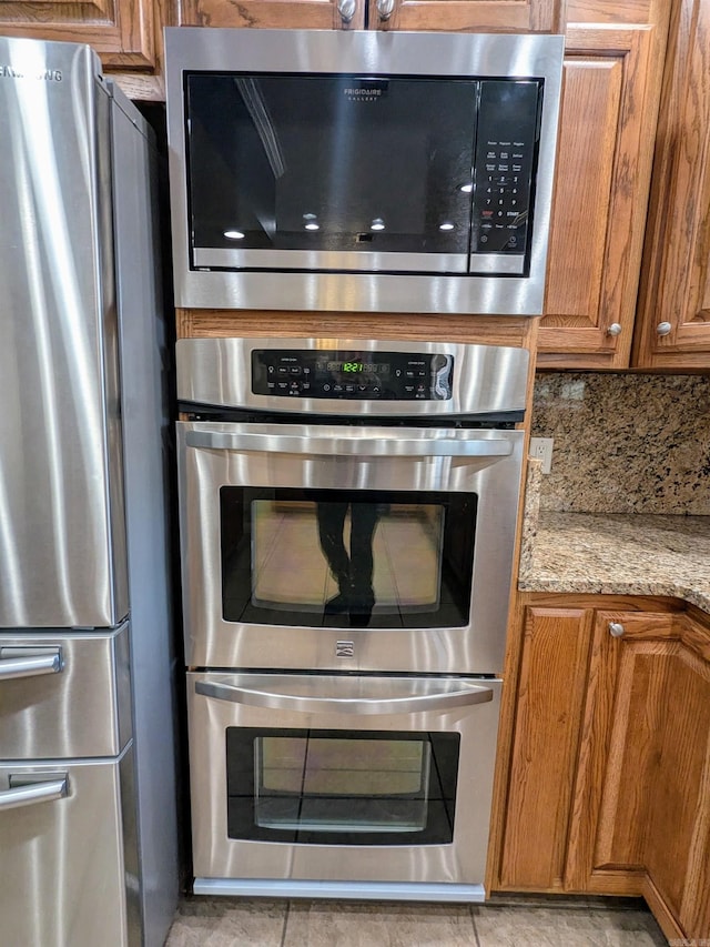 kitchen with stainless steel appliances, tasteful backsplash, light stone countertops, and light tile patterned flooring