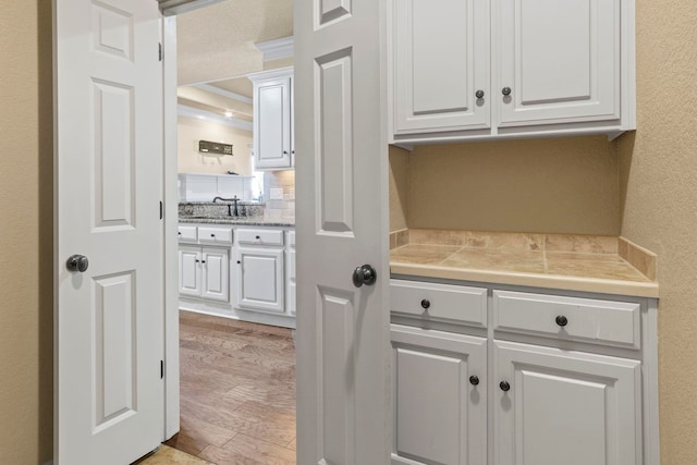 kitchen with white cabinetry, sink, crown molding, and light hardwood / wood-style floors