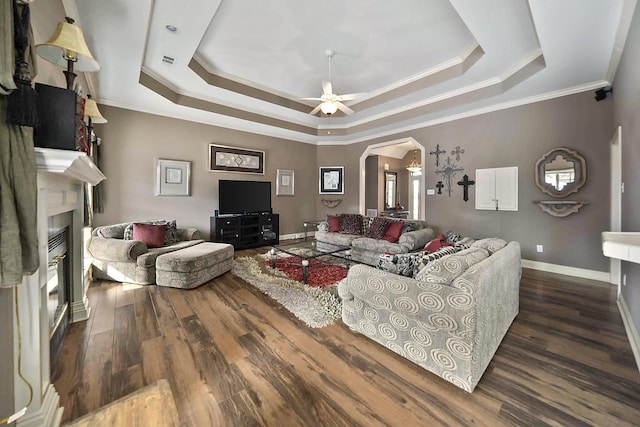 living room featuring a raised ceiling, ornamental molding, ceiling fan, and a fireplace