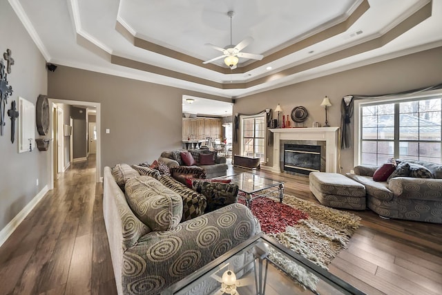 living room featuring crown molding, ceiling fan, a tray ceiling, wood-type flooring, and a tiled fireplace