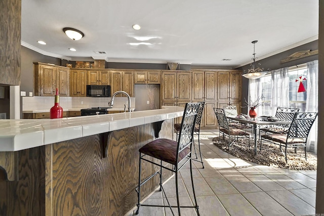 kitchen with pendant lighting, tasteful backsplash, light tile patterned floors, black appliances, and crown molding