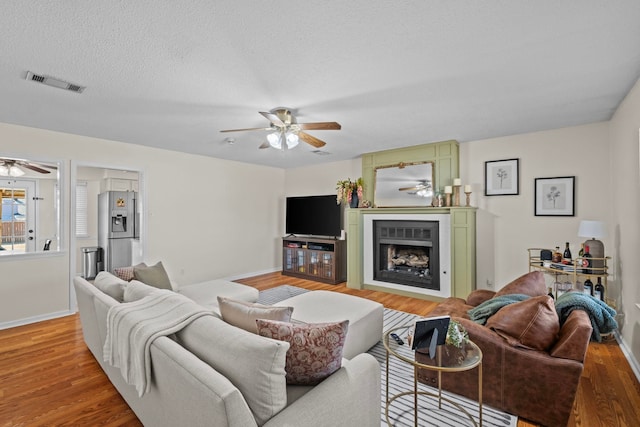 living room with hardwood / wood-style flooring, a fireplace, a textured ceiling, and ceiling fan