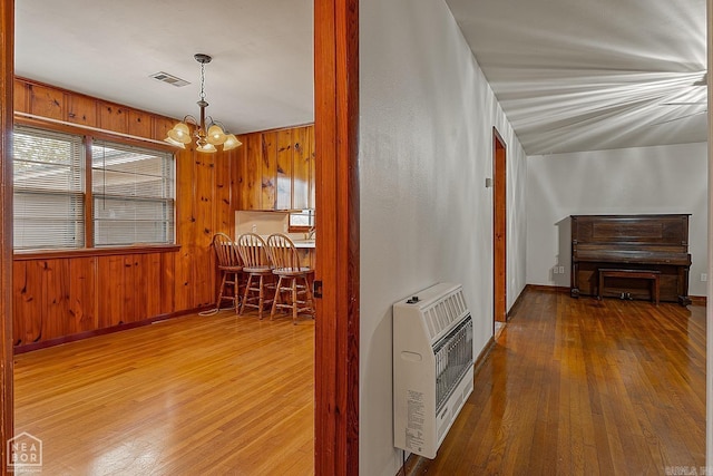 corridor with hardwood / wood-style floors, heating unit, and a notable chandelier