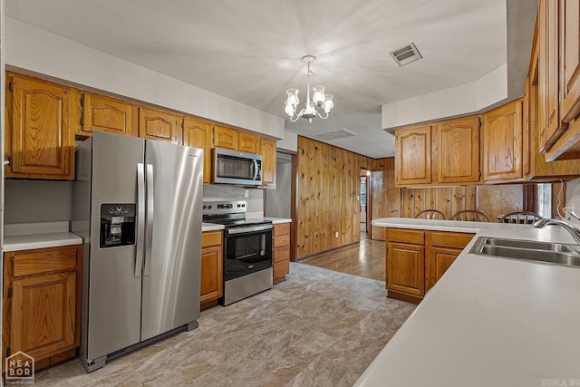 kitchen featuring pendant lighting, wood walls, sink, stainless steel appliances, and an inviting chandelier