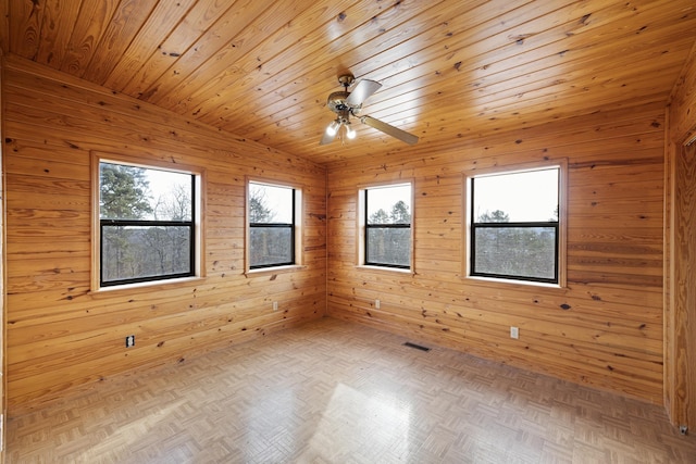 unfurnished room featuring vaulted ceiling, parquet flooring, a healthy amount of sunlight, and wood walls