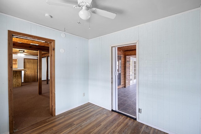 unfurnished room with dark hardwood / wood-style floors, ceiling fan, and wood walls