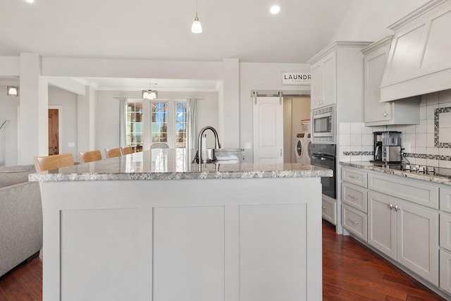 kitchen featuring washer and dryer, decorative light fixtures, black appliances, dark wood-type flooring, and custom range hood